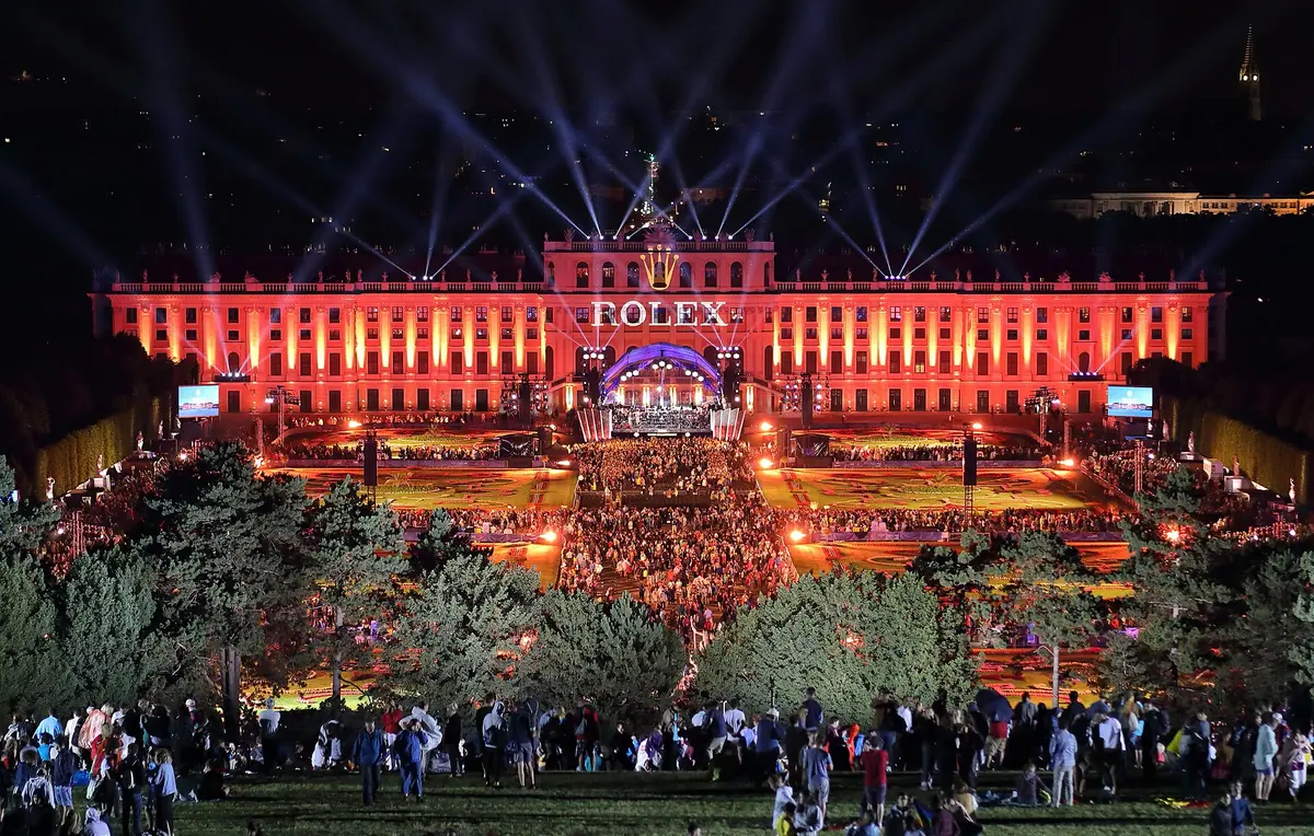 Gün batımı ışığında açık havada toplanmış, konser başlamasını bekleyen bir kalabalık